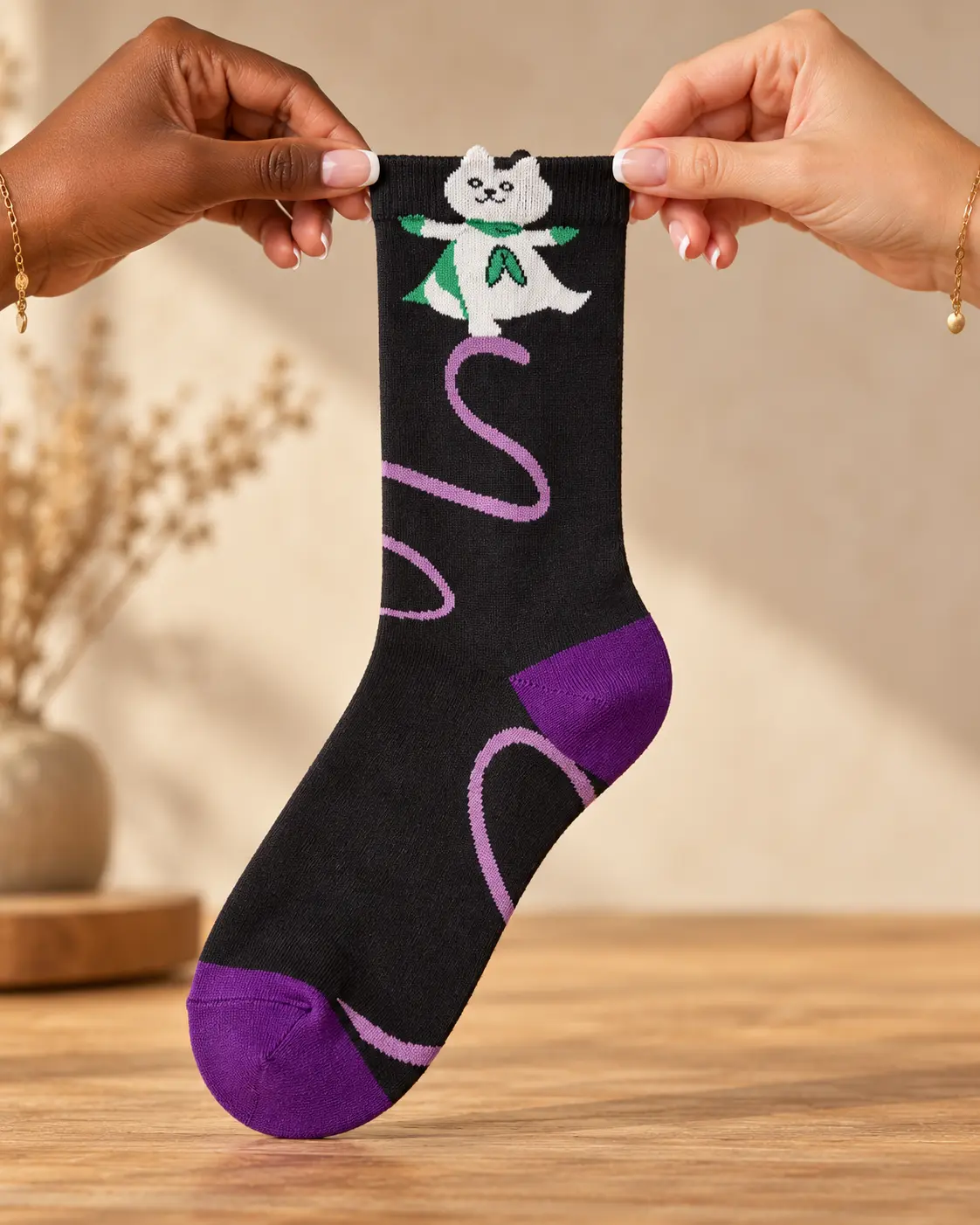Black socks with cat, green cape and purple details — held in hands